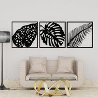 Set of three black leaf wall art frames above a blue sofa
