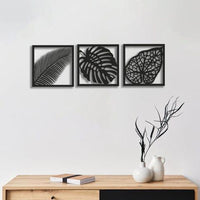 Black leaf wall art set of three displayed above a cream sofa